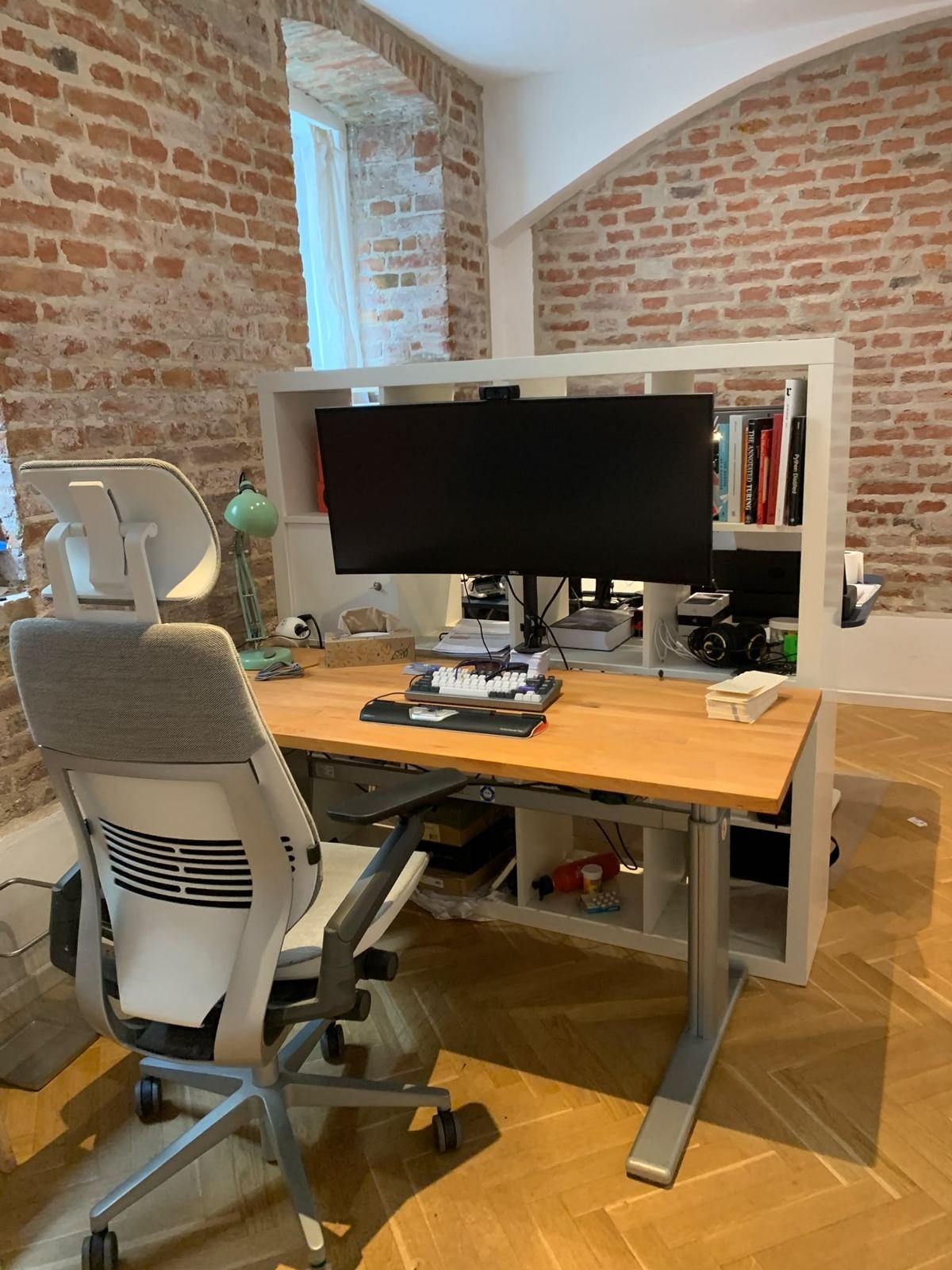 Arbeitsplatz mit Holztisch und ergonomischem Stuhl vor Ziegelwand und Gewölbe
